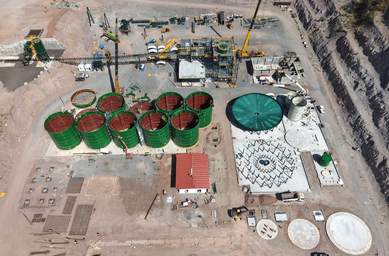 The image depicts a construction site with several large, cylindrical storage tanks surrounded by heavy machinery and construction materials.
AI-generated content may be incorrect.
