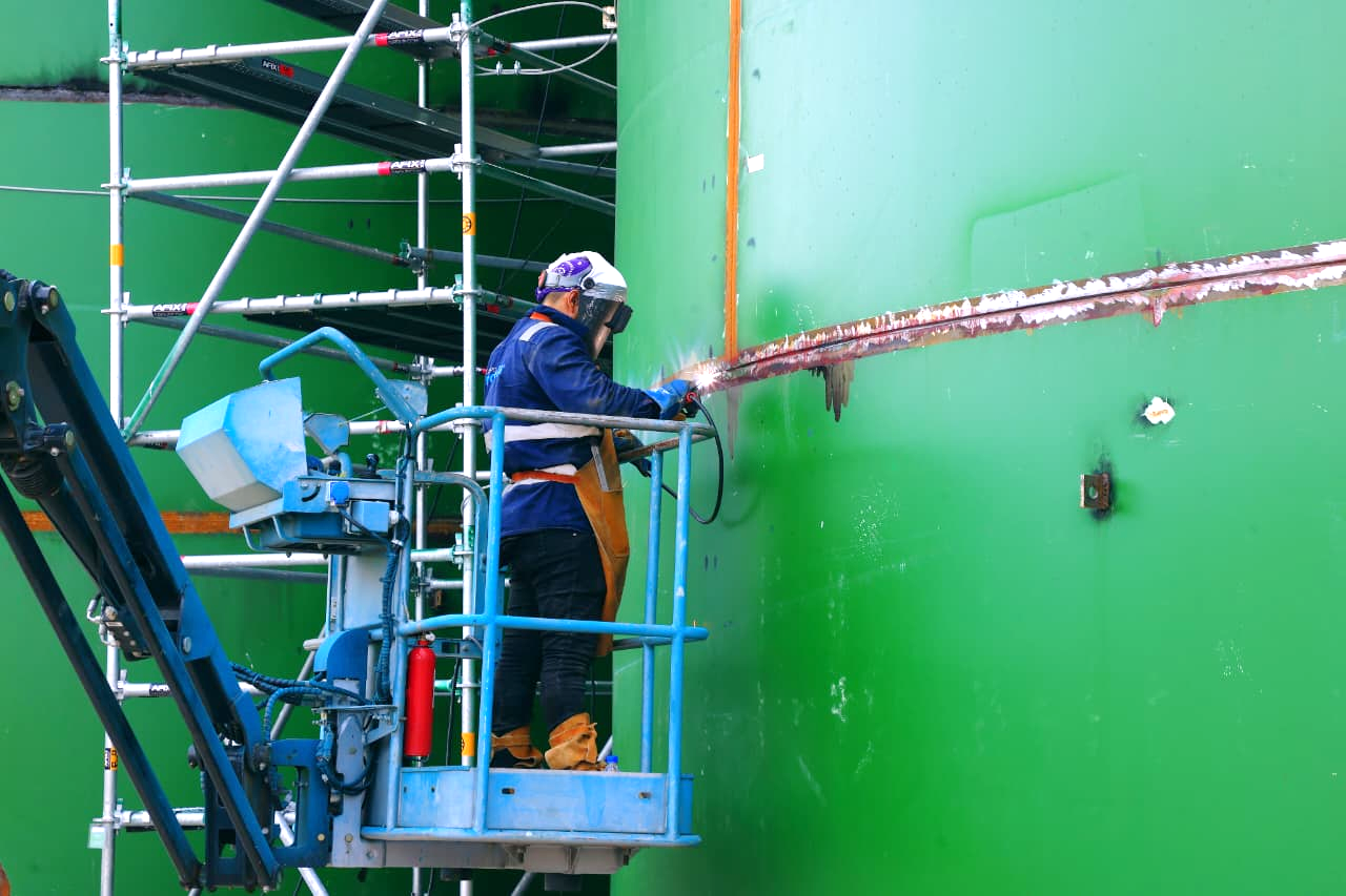 A construction worker is painting a large green wall, wearing a hard hat and safety gear.

AI-generated content may be incorrect.