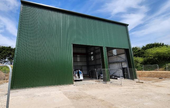 The image depicts a green metal storage shed with a tarp and a few storage containers, under a clear sky with some trees in the background.

AI-generated content may be incorrect.