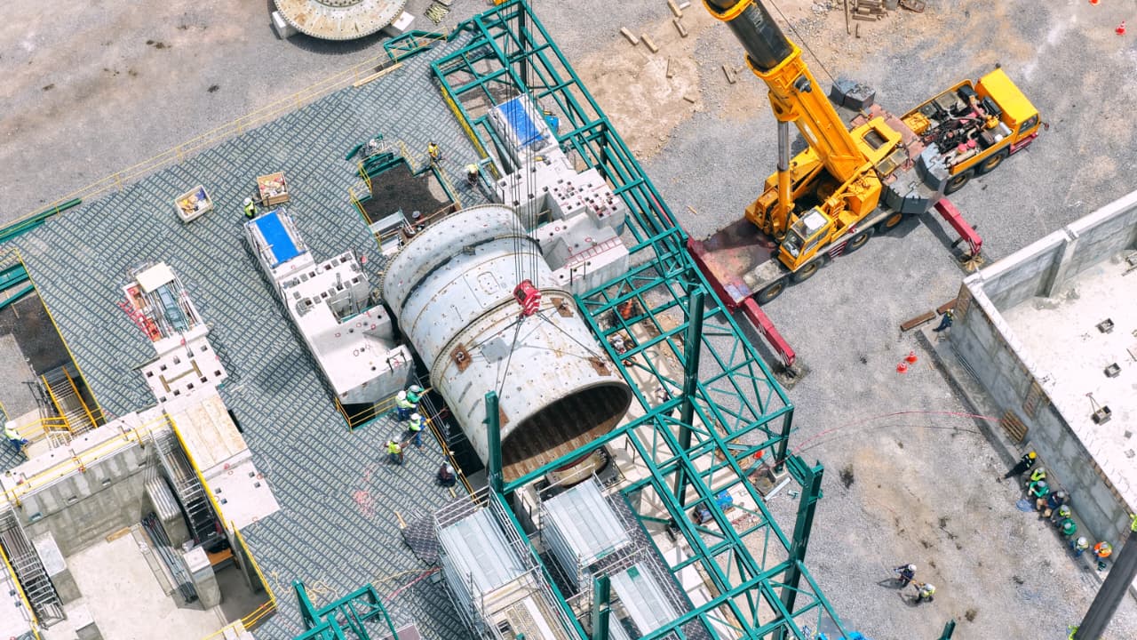 The image shows a construction site with a large crane lifting heavy machinery, surrounded by workers and equipment.

AI-generated content may be incorrect.