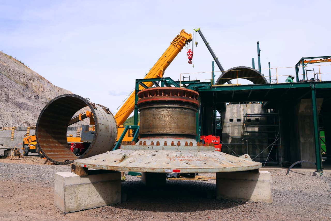 The image depicts a large, heavy industrial cement kiln, surrounded by construction equipment, with a crane lifting a large cylinder above it.
AI-generated content may be incorrect.